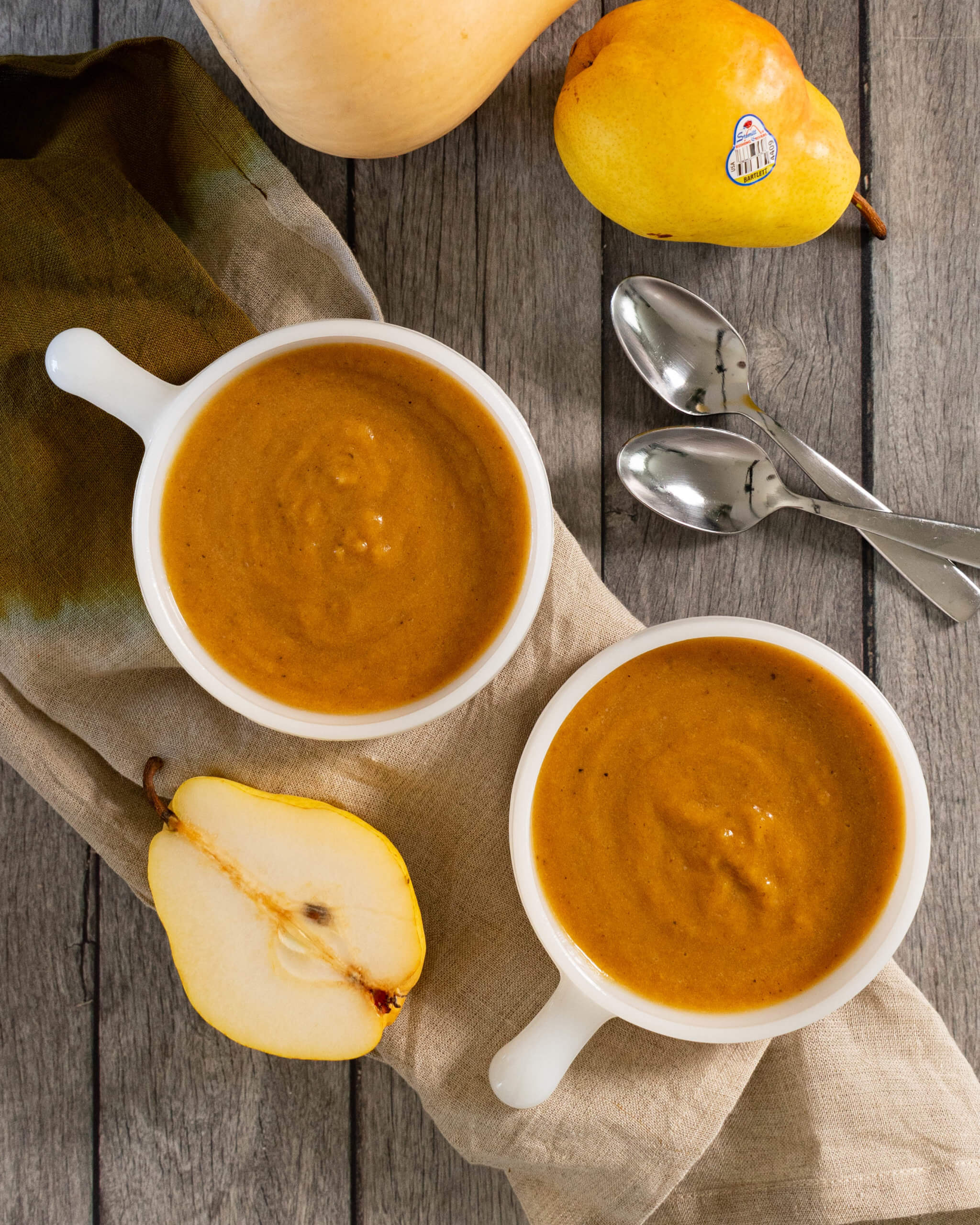 Finished Roasted Pear and Butternut Squash Soup in two bowls with pears and spoons on the side for decoration.