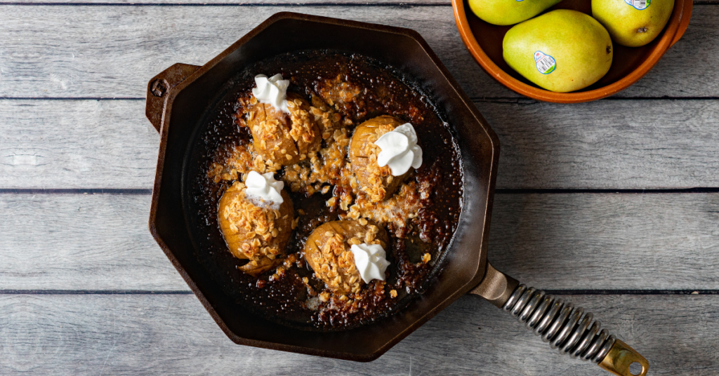 Hasselback pears coming out of the oven in a cast iron pan with whipped cream.