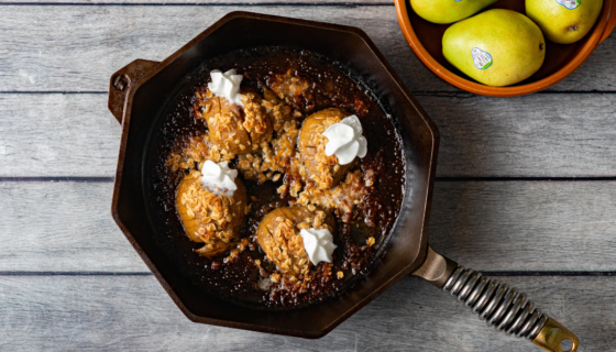 Hasselback pears coming out of the oven in a cast iron pan with whipped cream.