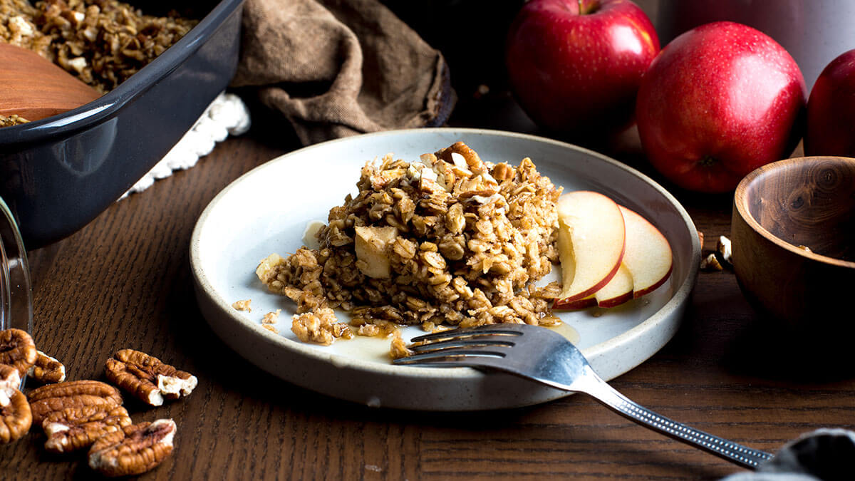 Baked oatmeal with apples and pecans on a plate with ingredients in the background.