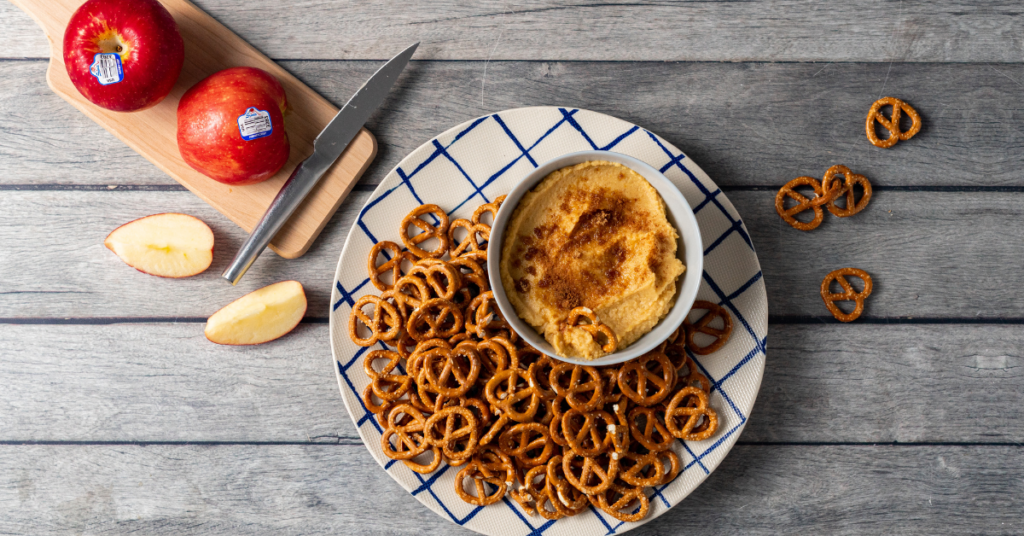 Apple butter hummus on a plate with pretzels. Pink Lady apples are on the side.