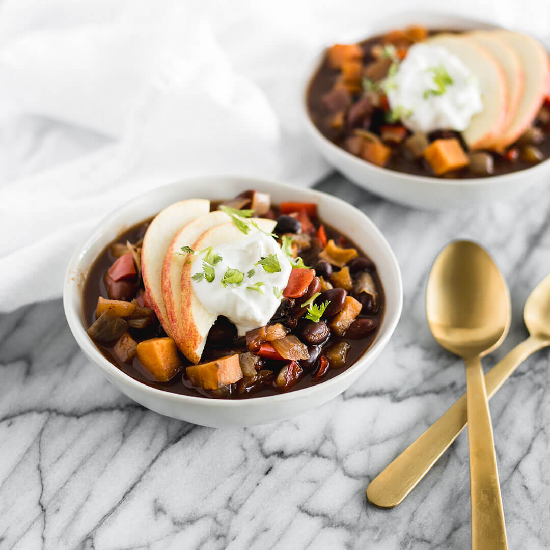 Two bowls of apple and sweet Potato chili with toppings and spoons.