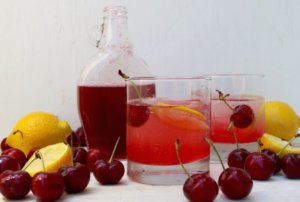 Cherry syrup in glass jug next to pink drink with cherries