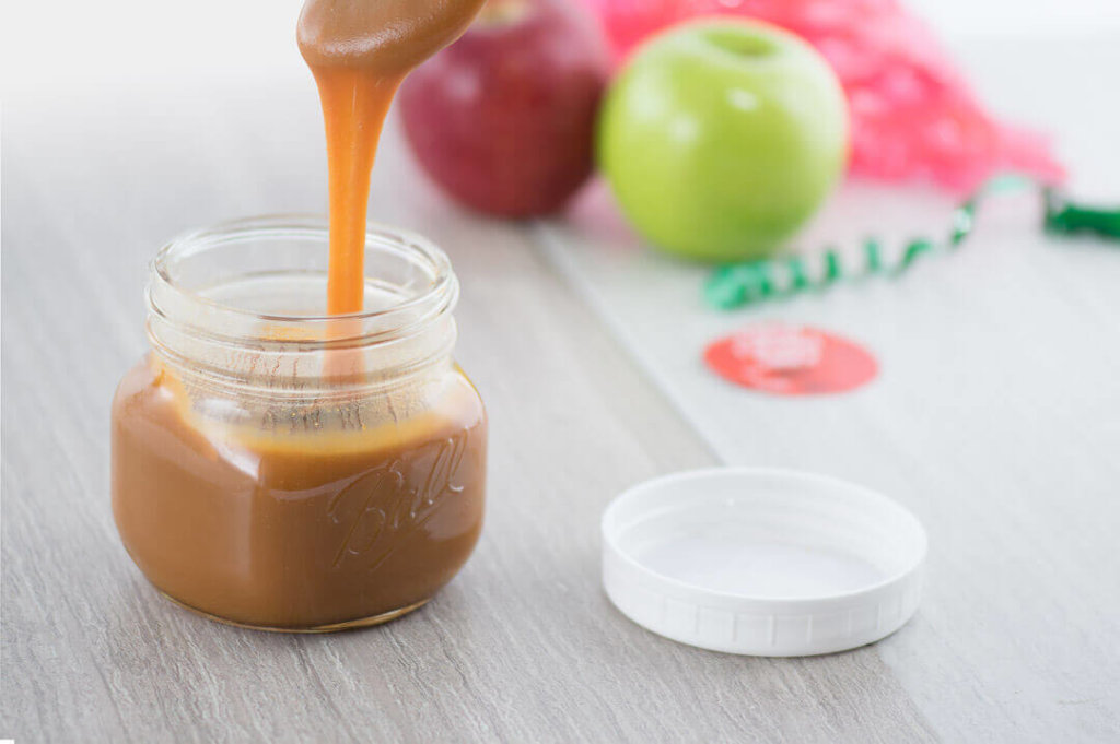 salted caramel sauce in a glass jar in the foreground, red and green apple in the background
