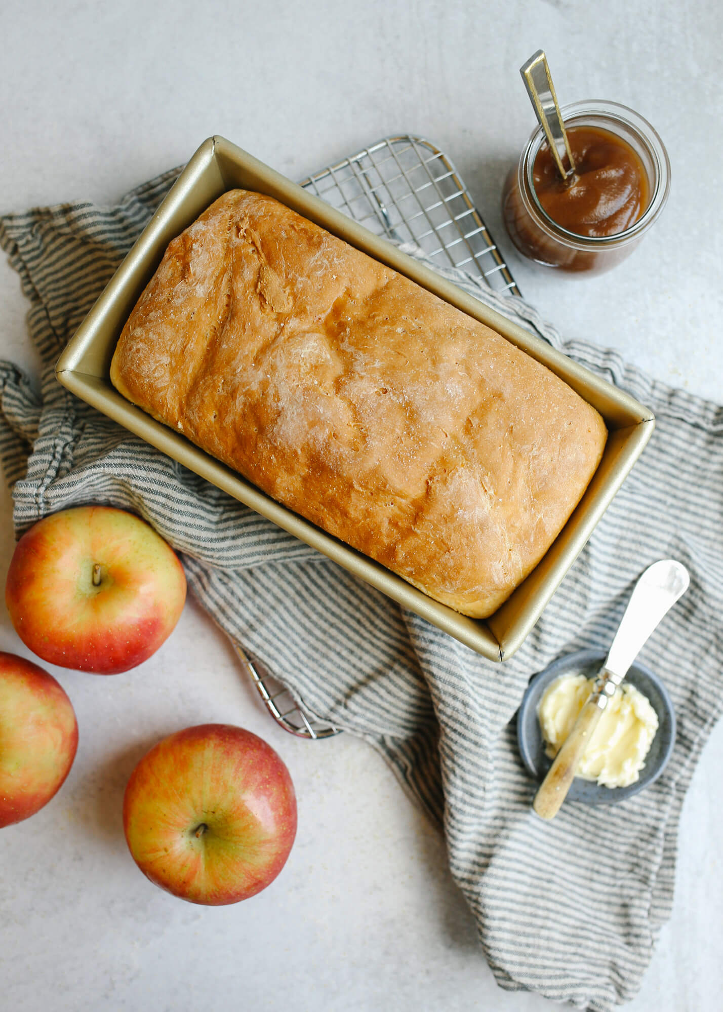 English Muffin Bread in loaf pan with apples and butter sitting around it.
