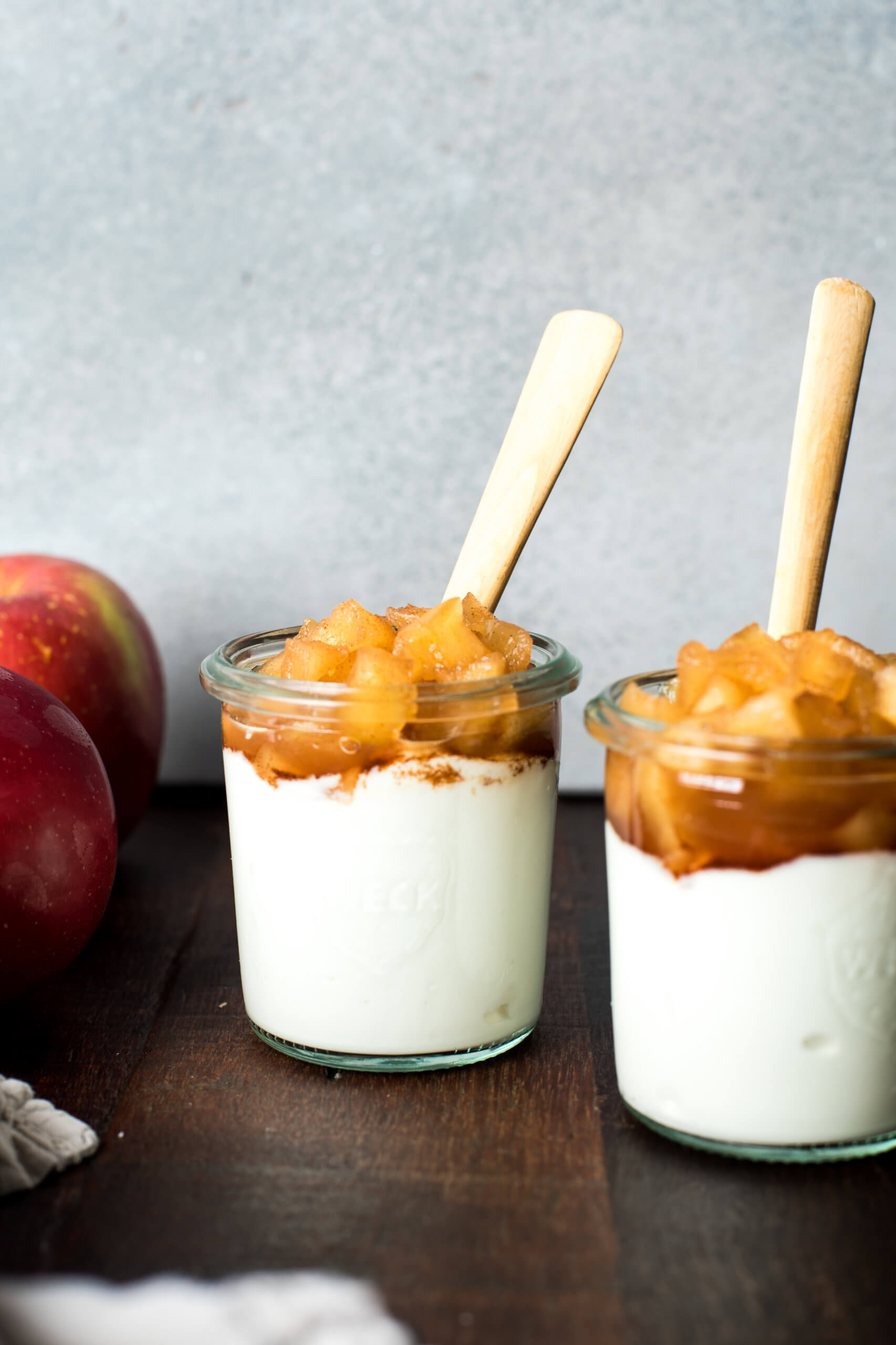 Yogurt parfaits with cinnamon apples on top, displays in a cup with spoons.