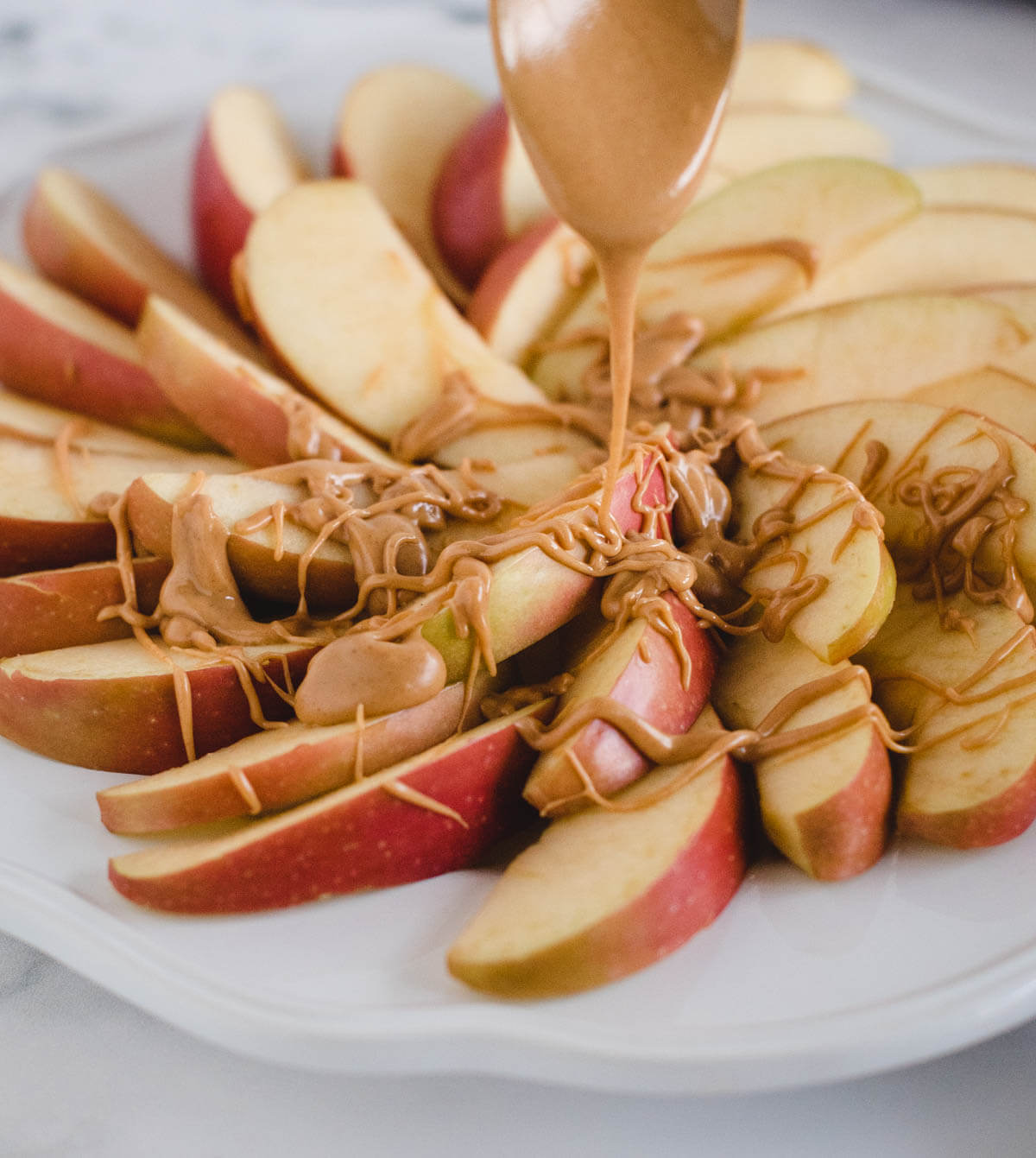 Sliced apples on a plate with peanut butter sauce drizzled on top.