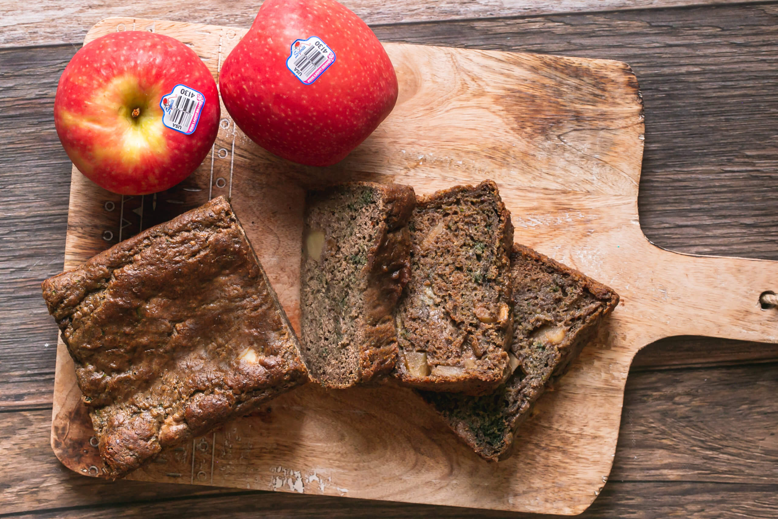 Zucchini Apple Cinnamon Bread cut into slices on a serving board with Pink Lady Apples next to it.