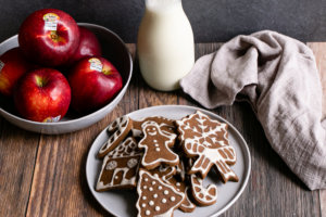 Gingerbread cookies on a plate with Cosmic Crisp apples and milk in the background