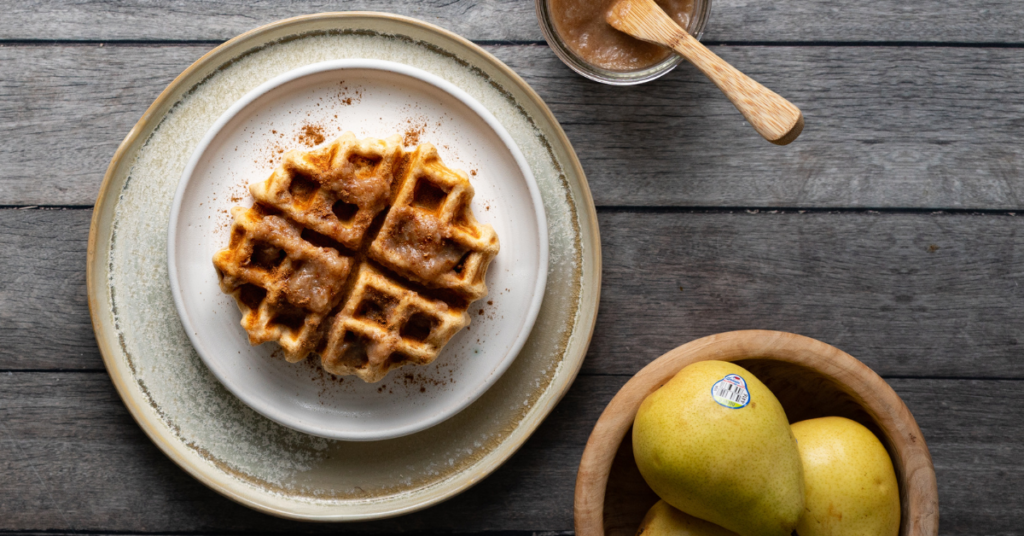 A plate of waffle with pear butter and pears in bowl next to the waffles