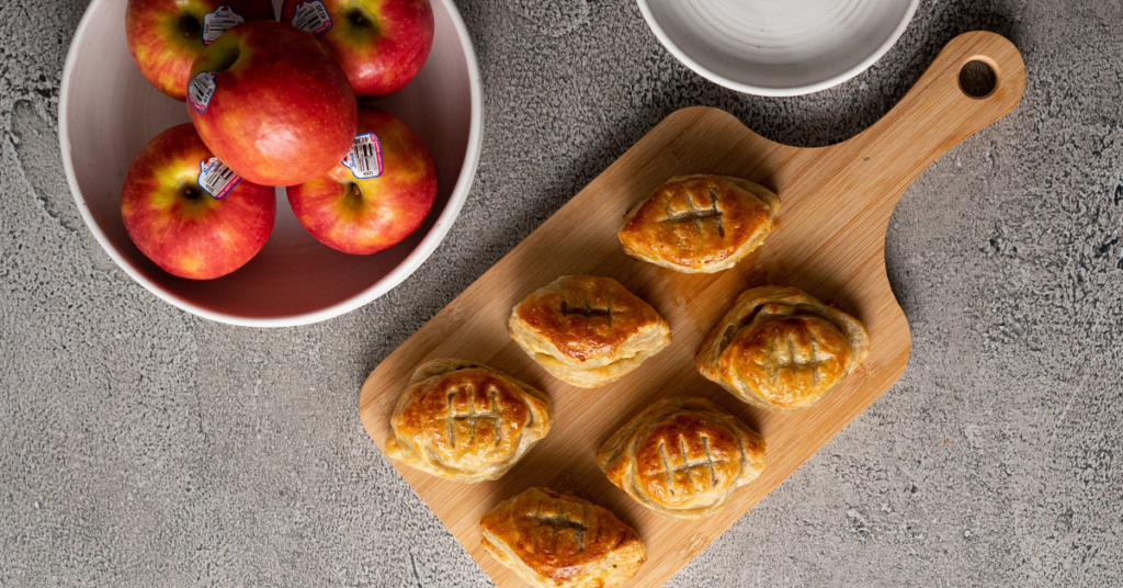 Apple Puff Bites on a cutting board. A bowl of pink lady apples sits on table next to the apple bites.