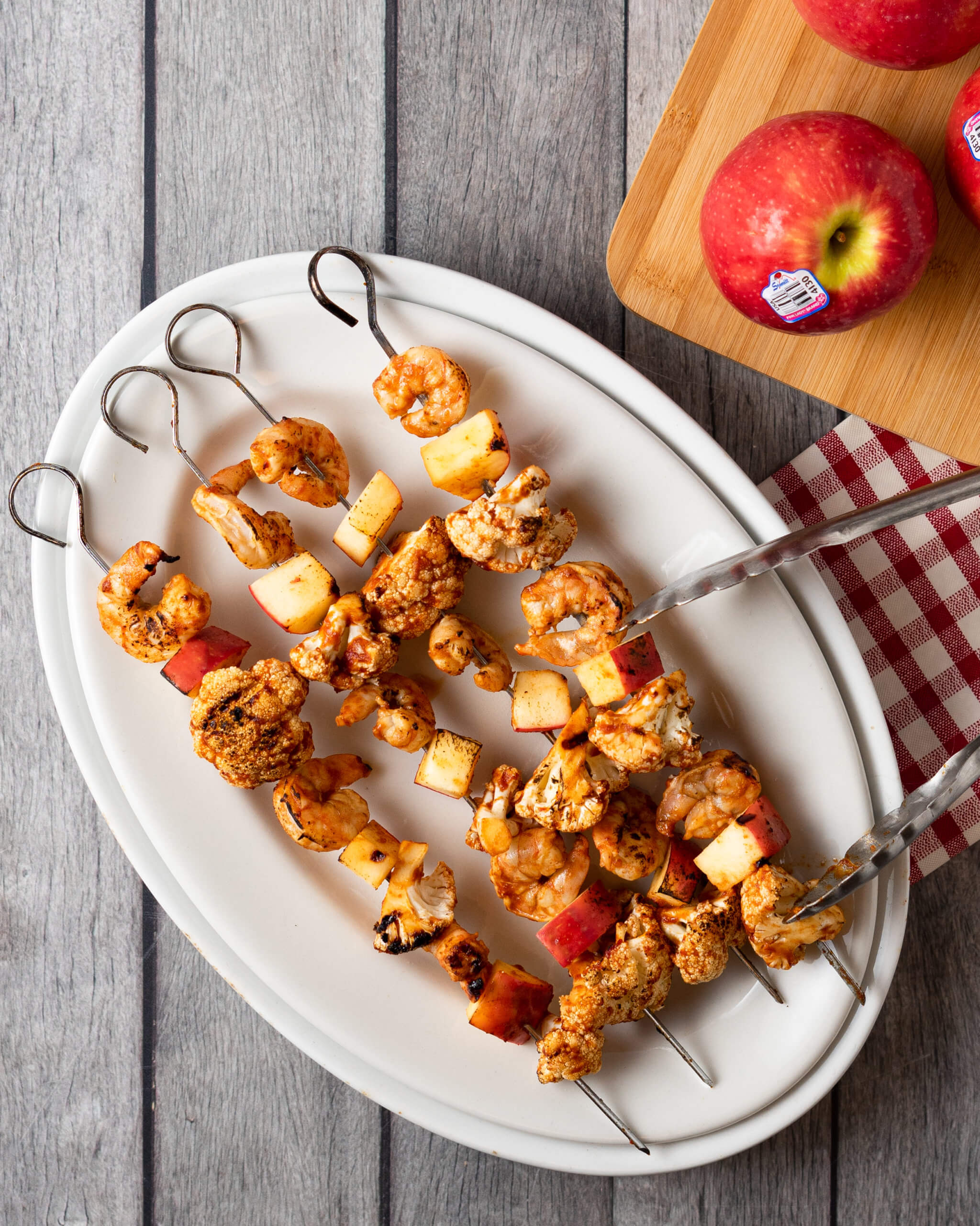 Apple shrimp cauliflower skewers on a white place, next to cutting board with apples