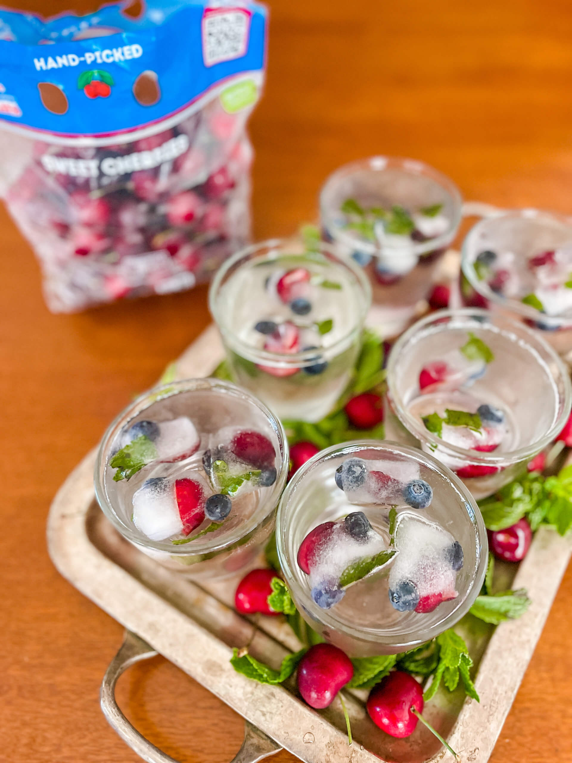 A tray with glasses of water and Cherr-Berry fruit ice cubes and a bag of Stemilt cherries in the background