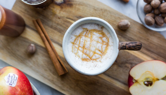 An Apple Crisp Macchiato drink on a cutting board with spices and apples slices