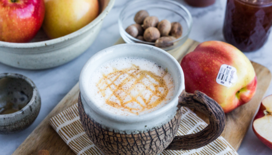 An Apple Crisp Macchiato displayed with whole apples and nutmeg spices