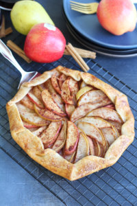 An Apple and Pear Galette on a cooling rack with apples and cinnamon in the background