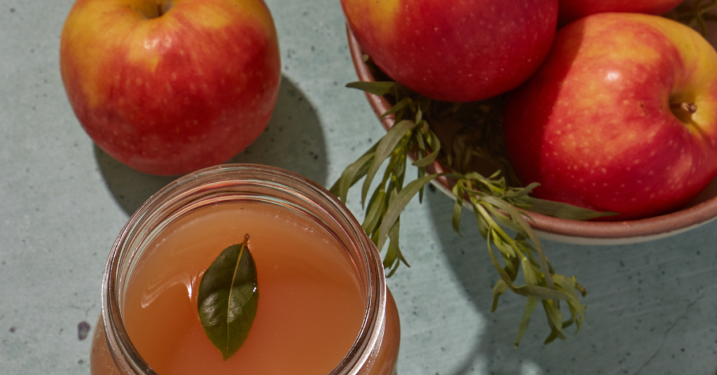 Apple cider in a jar with apples in a bowl besides it.