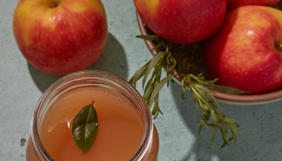 Apple cider in a jar with apples in a bowl besides it.