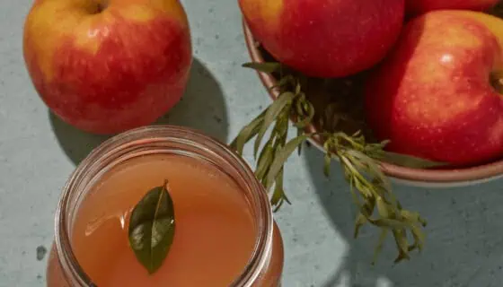 Apple cider in a jar with apples in a bowl besides it.