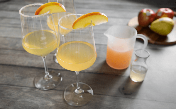 Apple & Pear Mimosas poured into tall glasses, with fruit and ingredients in the background