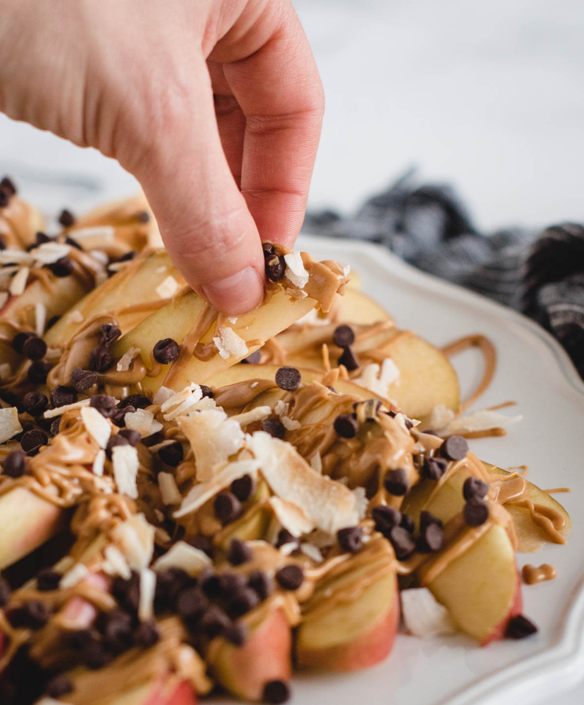A hand picking up a slice of apple drizzled with peanut butter and chocolate chips