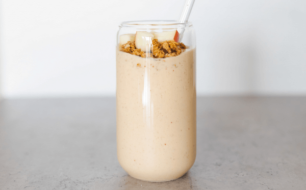 A healthy peanut butter and apple smoothie topped with granola and apple slices.