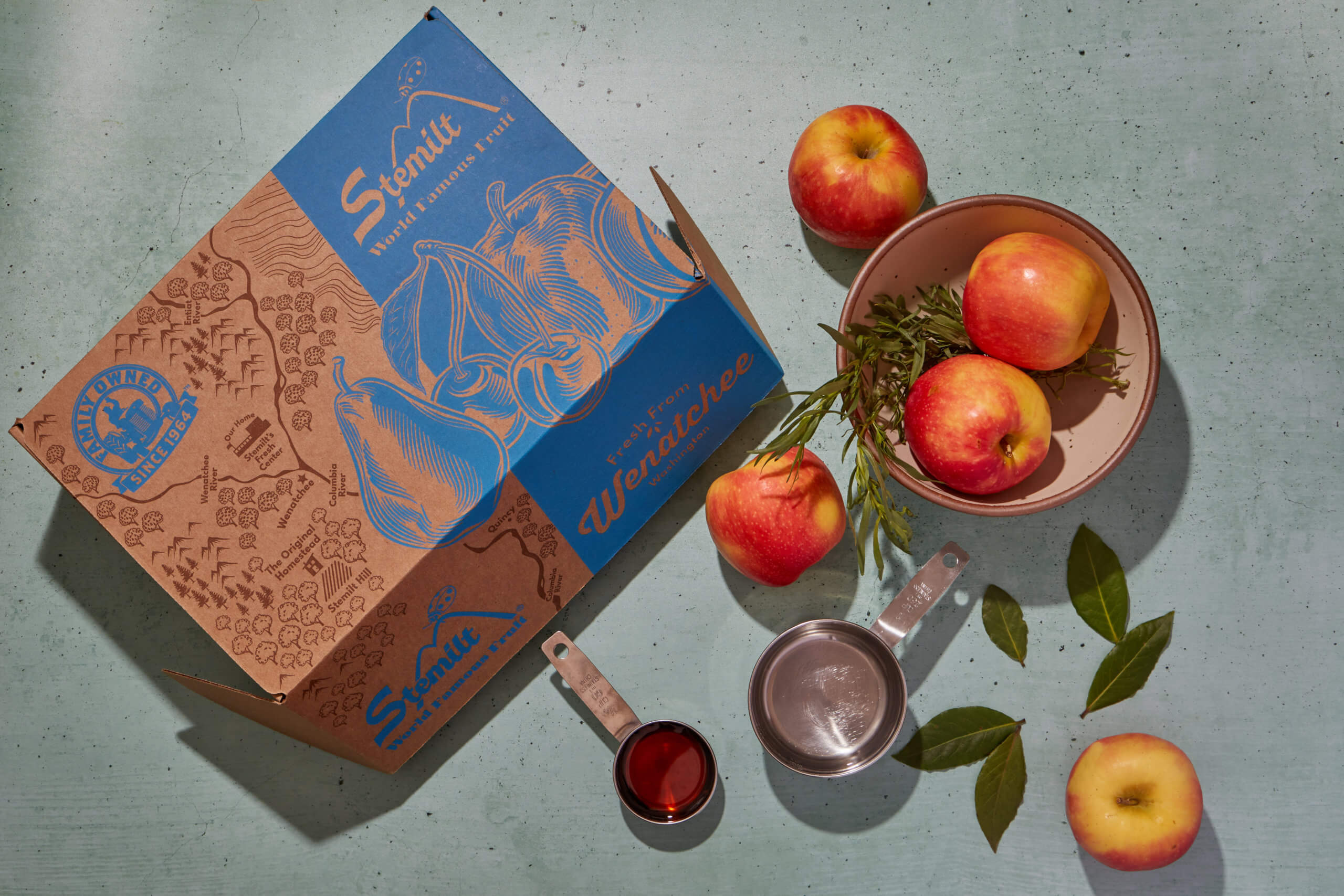 Apples with fresh bay leaves and rosemary, next to a Stemilt box.