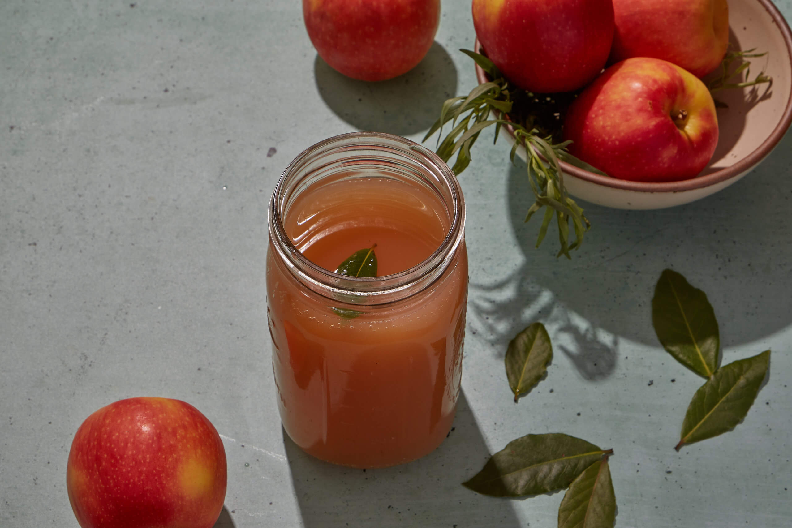 Apple cider in a mason jar with bay leaves, and apples next to it.