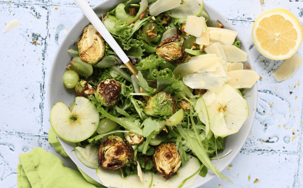 A spring salad featuring green ingredients- apples, brussels sprouts, spring mix