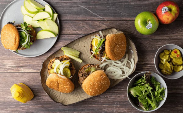 Plant based burgers on a tray with apple slices on the side.