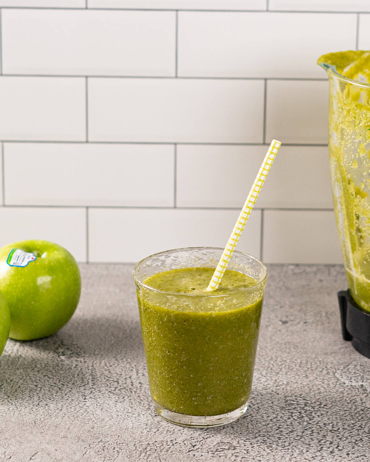 Green apple smoothie poured into a glass with a granny smith apple in the background.