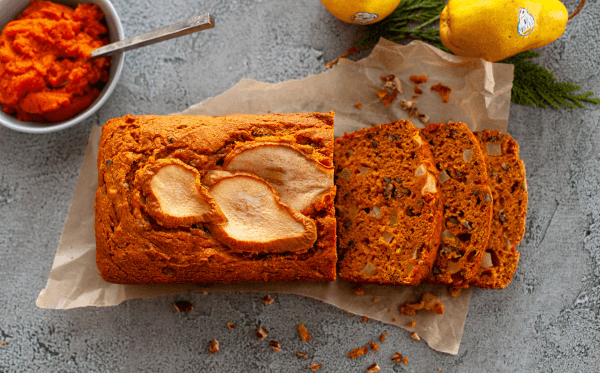 Pumpkin Pear Bread sliced on a counter next to fresh pumpkin and pears