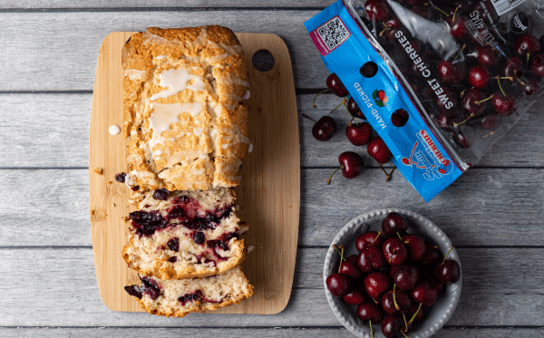 A sliced fresh cherry layered cake loaf with a bowl of fresh cherries on the side.