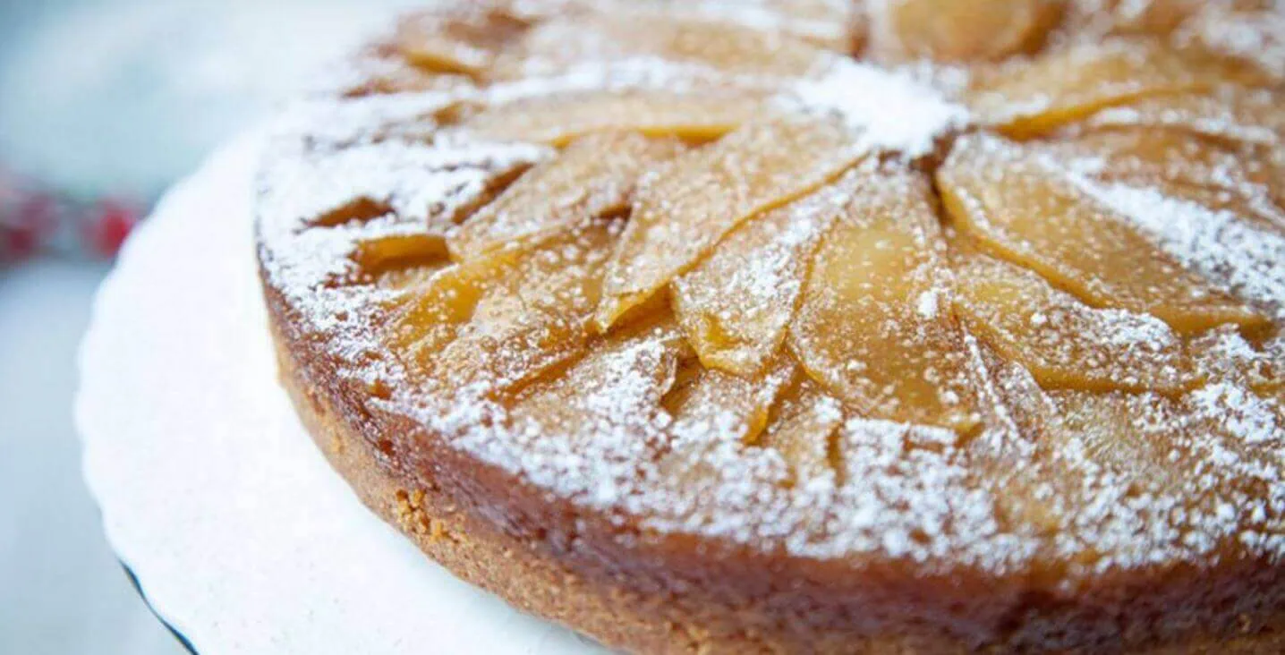 Close-up of a golden apple upside down cake with caramelized apple slices and powdered sugar.