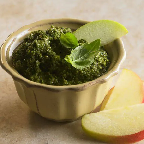 Apple pesto in a small bowl garnished with basil and apple slices.