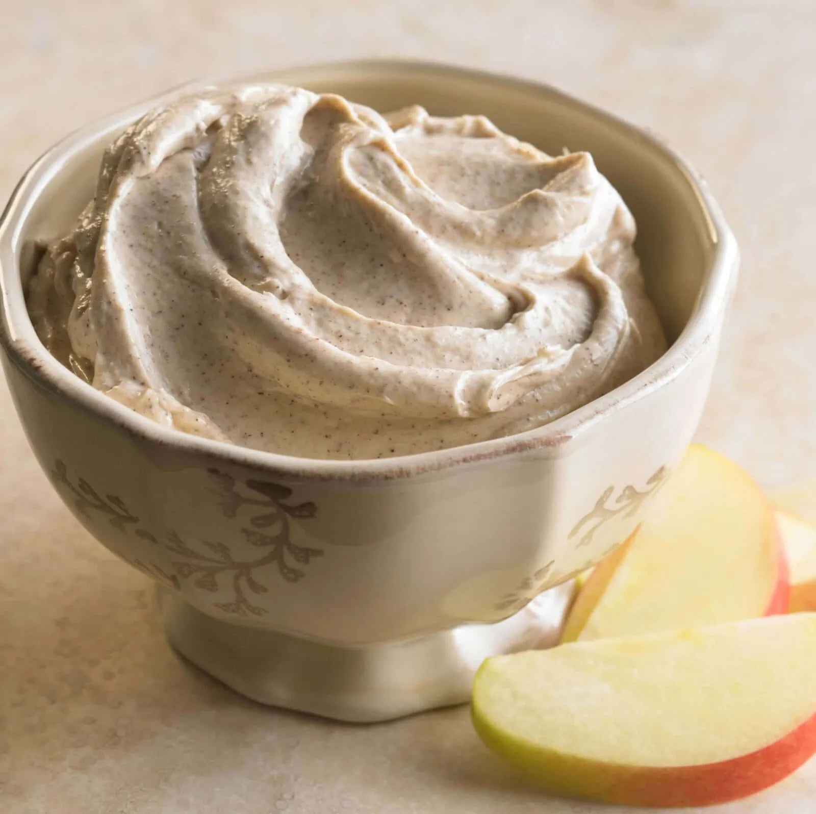 Creamy cinnamon and honey apple dip in a decorative bowl with apple slices nearby.