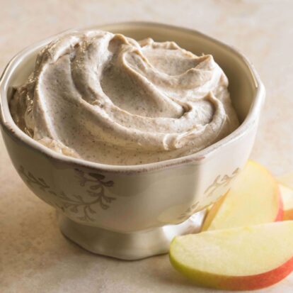 Creamy cinnamon and honey apple dip in a decorative bowl with apple slices nearby.