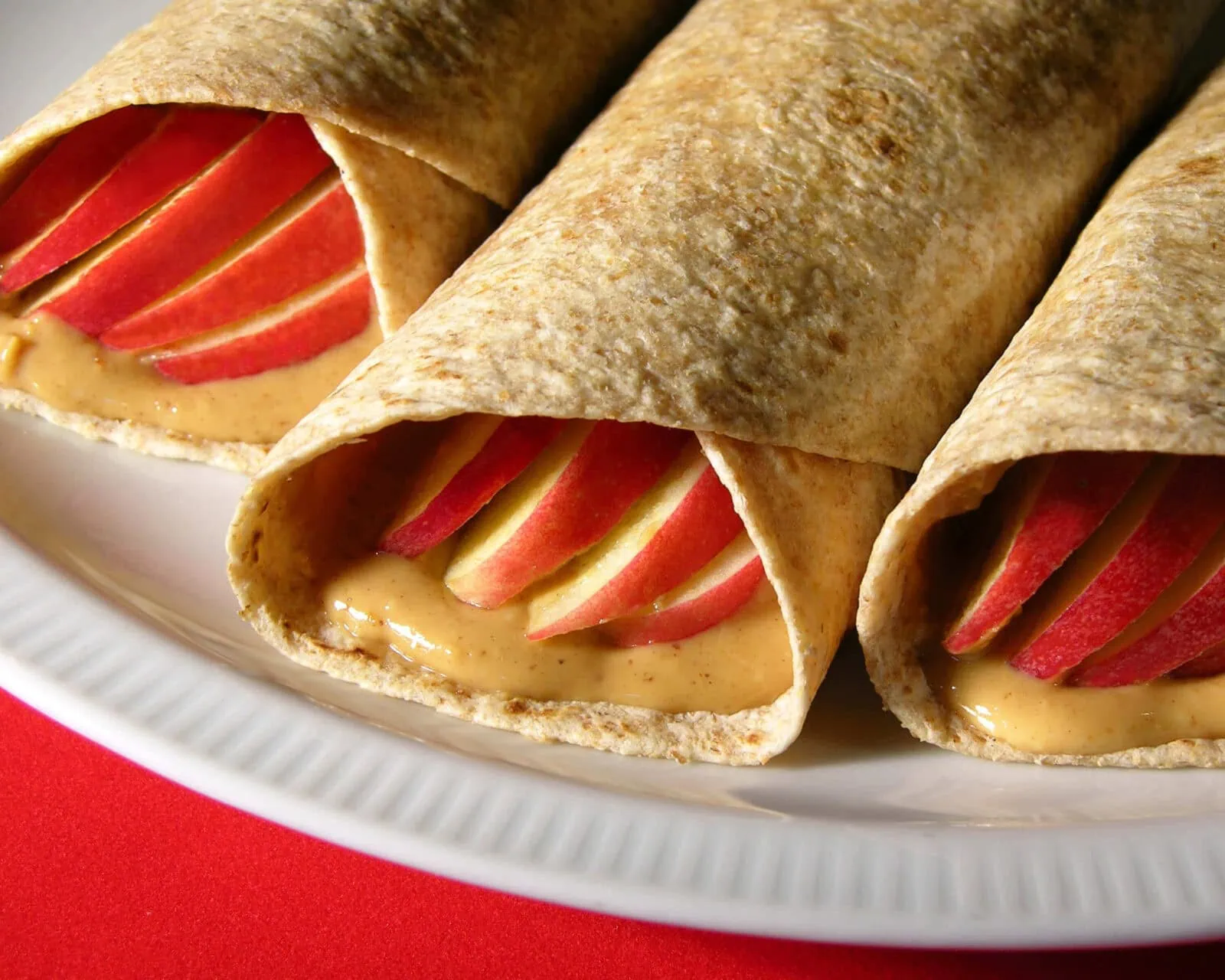 Apple and peanut butter wraps with sliced apples inside on a white plate.