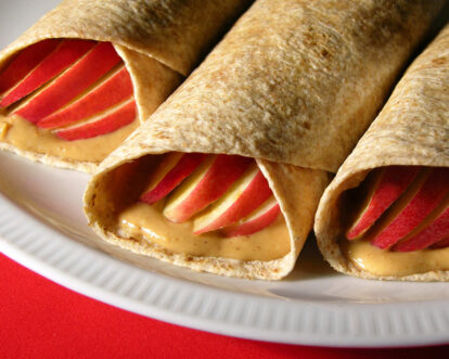 Apple and peanut butter wraps with sliced apples inside on a white plate.