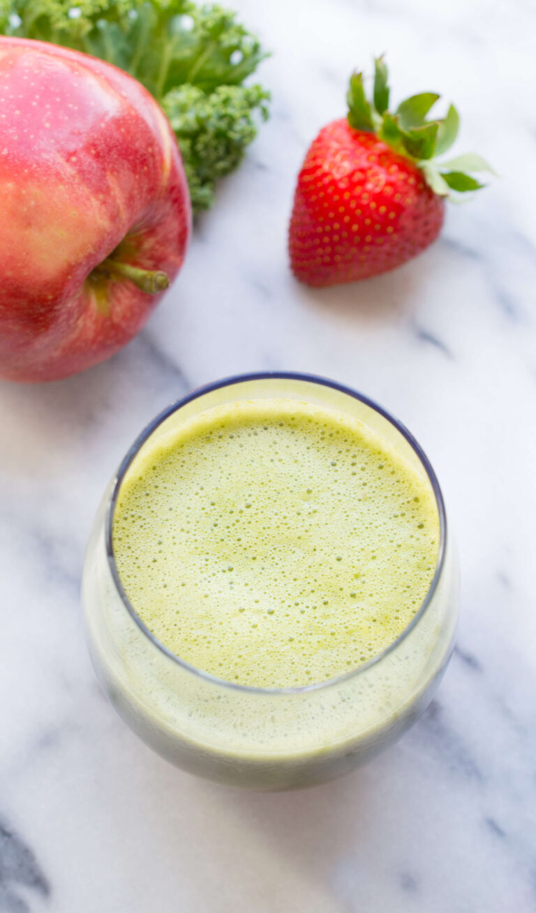 Fresh strawberry, apple, kale, and green juice in a glass on marble surface.