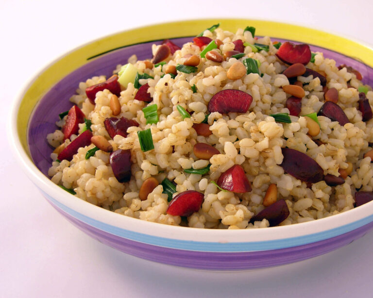 Cherry and brown rice pilaf in colorful bowl with green onions and nuts.