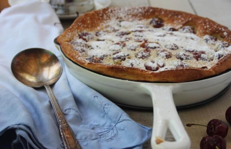 Classic cherry clafouti with powdered sugar and fresh cherries on top.