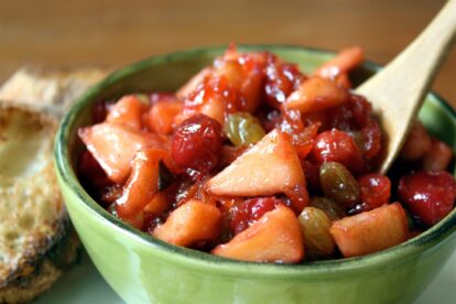 Cherry and apple chutney in a green bowl with a wooden spoon.