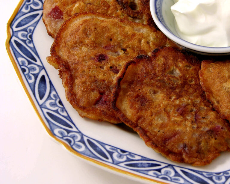 Close-up of cherry fritters with whipped cream on a decorative plate.