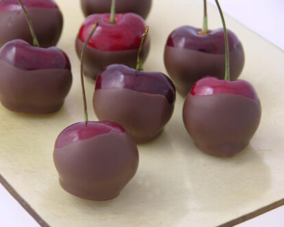 Cherries dipped in chocolate on a white platter for dessert or snack.