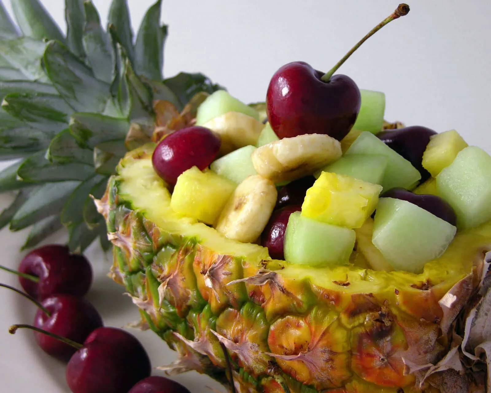 Fresh pineapple bowl filled with cherries, melon, and banana chunks for a fruit salad.