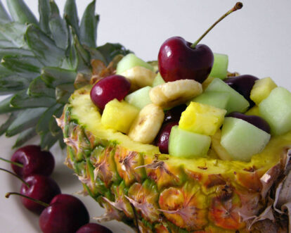 Fresh pineapple bowl filled with cherries, melon, and banana chunks for a fruit salad.