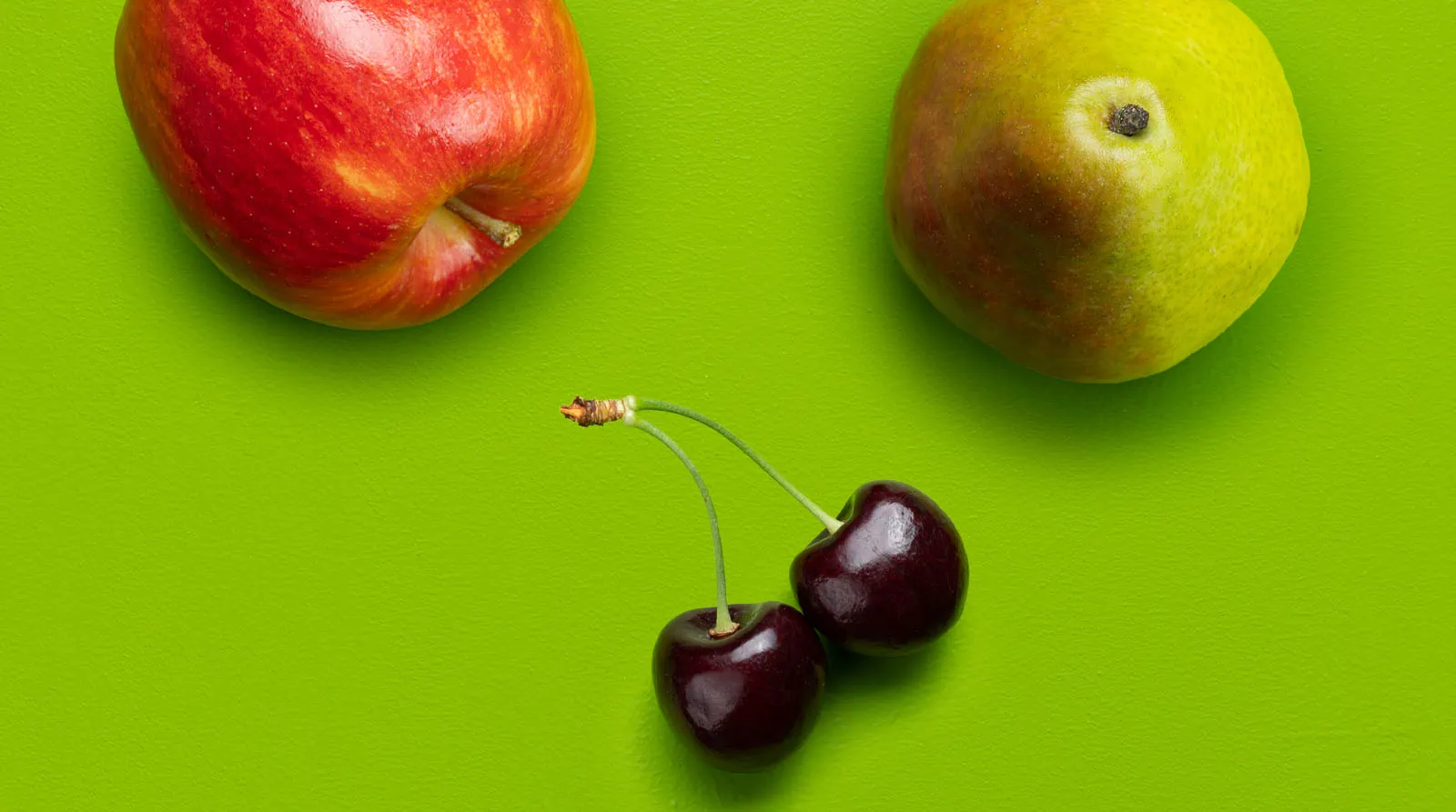 Fresh organic apple, pear, and cherries on bright green background.