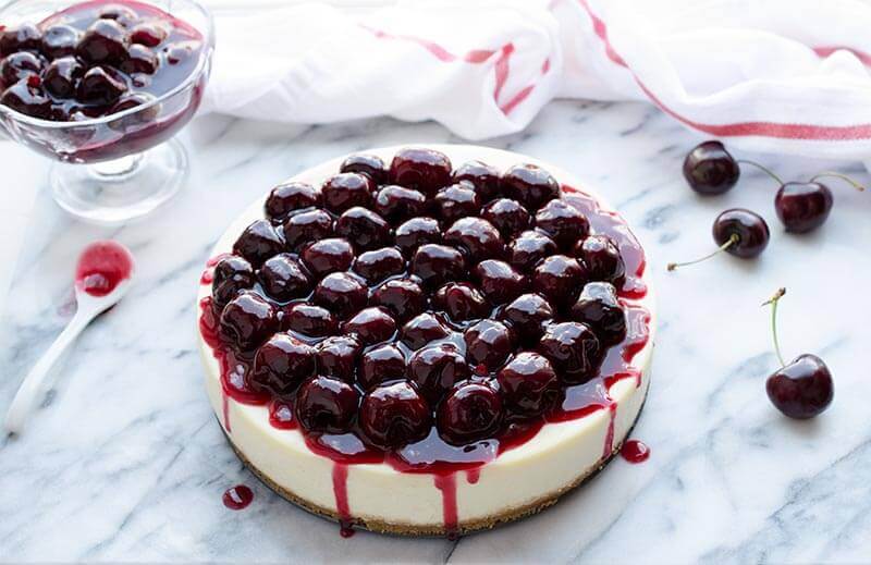 Cherry cheesecake topped with fresh cherries on a marble surface.