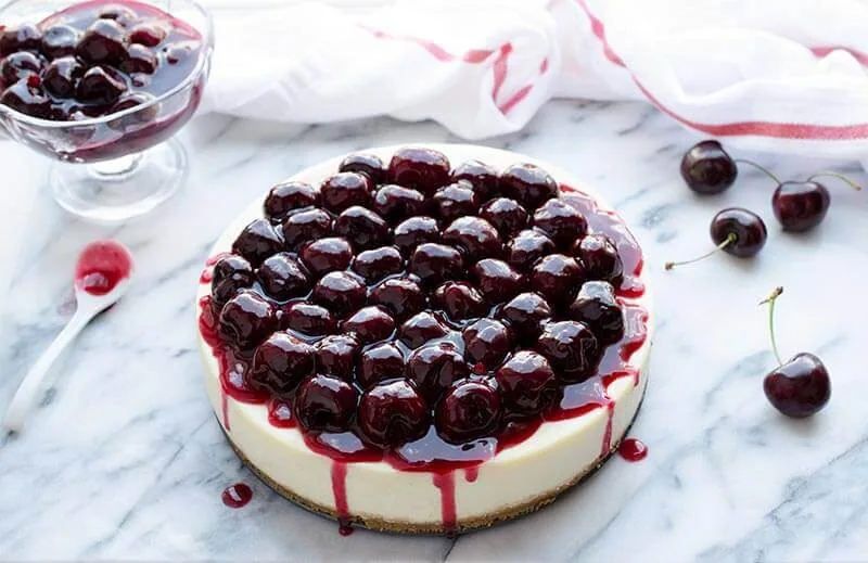 Cherry cheesecake topped with fresh cherries on a marble surface.
